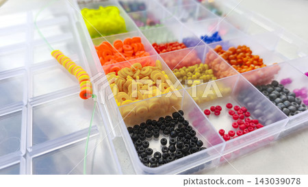 Close-up view of assorted craft beads in vibrant colors organized in a transparent compartment tray, representing creativity, DIY accessories, jewelry making and artistic hobbies. Selective focus Close-up view of assorted craft beads in vibrant colors organized in a transparent compartment tray, representing creativity, DIY accessories, jewelry making and artistic hobbies. Selective focus 143039078