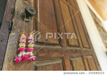 Traditional Thai flower garland made of pink, white and multicolored blossoms hangs from an antique brass door handle on a rustic wooden door, symbolizing good fortune and blessing Traditional Thai flower garland made of pink, white and multicolored blossoms hangs from an antique brass door handle on a rustic wooden door, symbolizing good fortune and blessing 143040315