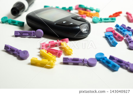 Digital glucometer surrounded by colorful lancets on white background Digital glucometer surrounded by colorful lancets on white background 143040927