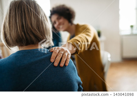 Woman offering comforting touch to another participant during group therapy session. 143041098