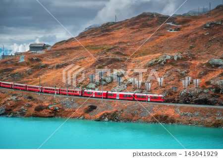 Aerial view of red train near alpine mountain lake and cloudy sky Aerial view of red train near alpine mountain lake and cloudy sky 143041929