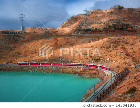 Aerial view of red train near alpine mountain lake and cloudy sky Aerial view of red train near alpine mountain lake and cloudy sky 143041933