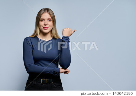 Smiling young woman pointing thumb to copy space studio Smiling young woman pointing thumb to copy space studio 143042190