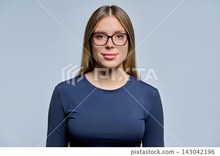 Young woman in eyeglasses looking at camera on studio gray background Young woman in eyeglasses looking at camera on studio gray background 143042196