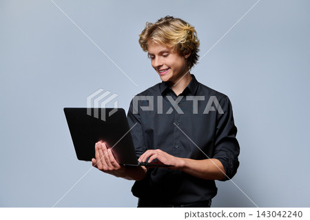Smiling young male student typing on laptop computer against grey background Smiling young male student typing on laptop computer against grey background 143042240