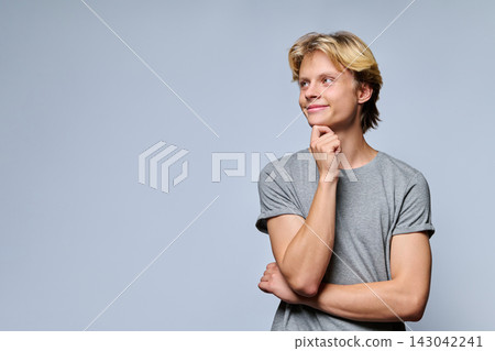Thoughtful teenage boy holding hand on chin looking away on grey background 143042241