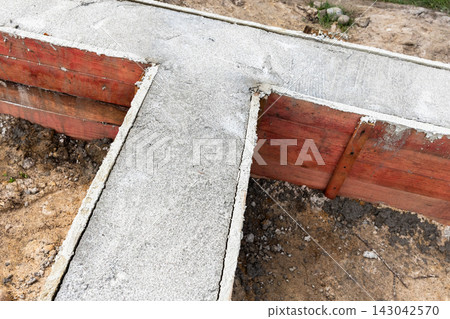 Concrete foundation footings poured into wooden formwork Concrete foundation footings poured into wooden formwork 143042570