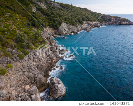 Rocky shoreline at aquarium bay albania borders deep blue water. Coastal cliffs rise above foaming waves, while green hillside growth adds remote, tranquil feel to this seaside landscape. Rocky shoreline at aquarium bay albania borders deep blue water. Coastal cliffs rise above foaming waves, while green hillside growth adds remote, tranquil feel to this seaside landscape. 143043271
