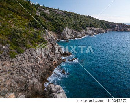 Rocky aquarium bay albania coastline meets clear blue water beside steep green cliffs. Coastal bay feels rugged and serene, with waves washing against limestone rocks under bright daylight. Rocky aquarium bay albania coastline meets clear blue water beside steep green cliffs. Coastal bay feels rugged and serene, with waves washing against limestone rocks under bright daylight. 143043272