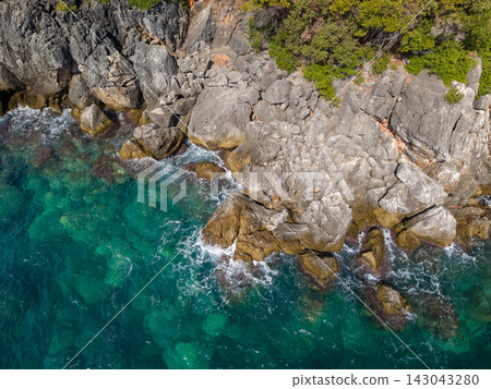 Rocky coast and clear water frame aquarium bay Albania. Turquoise sea laps rugged cliffs and boulders, giving coastal bay calm, natural feel with bright summer color and dramatic stone texture. Rocky coast and clear water frame aquarium bay Albania. Turquoise sea laps rugged cliffs and boulders, giving coastal bay calm, natural feel with bright summer color and dramatic stone texture. 143043280
