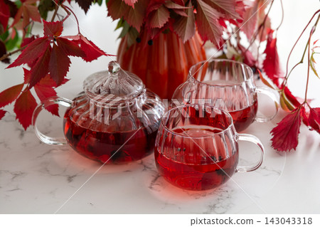 Autumn tea ritual cozy warm beverage in glass teapot and cups with red leaves decoration 143043318