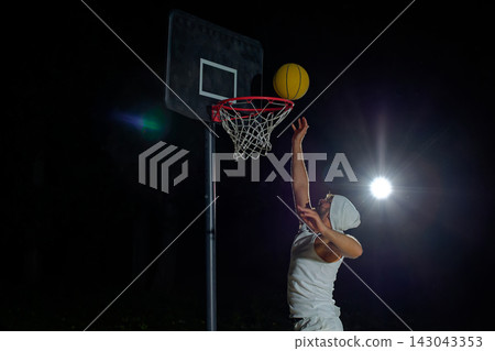 A man performs a slam dunk on a basketball court at night under the glare of bright outdoor lights A man performs a slam dunk on a basketball court at night under the glare of bright outdoor lights 143043353