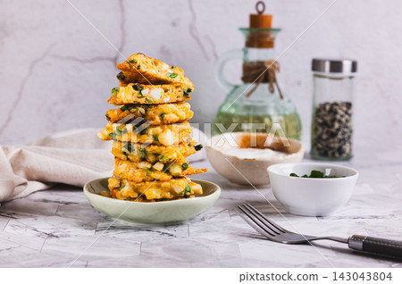 A stack of fried fritters with eggs, green onions, and cheese on a plate on the table. A stack of fried fritters with eggs, green onions, and cheese on a plate on the table. 143043804