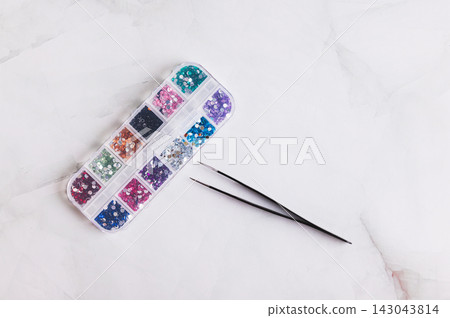 A box of assorted colorful decorative rhinestones and tweezers on the table top view A box of assorted colorful decorative rhinestones and tweezers on the table top view 143043814
