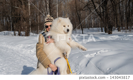 Smiling woman holding fluffy samoyed dog in snowy winter park. Smiling woman holding fluffy samoyed dog in snowy winter park. 143043817