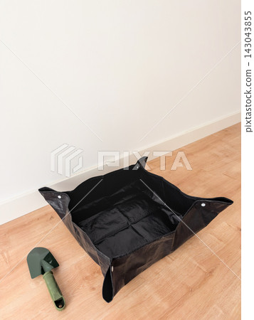 Black foldable repotting mat and green garden trowel on a wooden floor with white wall copy space Black foldable repotting mat and green garden trowel on a wooden floor with white wall copy space 143043855