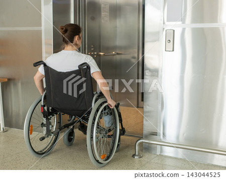 A Caucasian woman in a wheelchair uses an elevator. A Caucasian woman in a wheelchair uses an elevator. 143044525