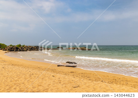 Tranquil tropical beach scene with golden sand, gentle ocean waves, and rocky outcrops under a soft, light blue sky, inviting relaxation. Sri Lanka island in Asia. Tranquil tropical beach scene with golden sand, gentle ocean waves, and rocky outcrops under a soft, light blue sky, inviting relaxation. Sri Lanka island in Asia. 143044623