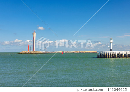 Coastal Harbor Scene on a Sunny Day with Lighthouses and Breakwater, Calm Sea and Blue Sky with Clouds. Ostend, a coastal city in Belgium, Europe. Coastal Harbor Scene on a Sunny Day with Lighthouses and Breakwater, Calm Sea and Blue Sky with Clouds. Ostend, a coastal city in Belgium, Europe. 143044625