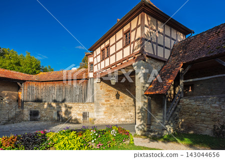 Rothenburg ob der Tauber, medieval old town in region of Bavaria in Germany, Europe. Historic Half-Timbered Building and Stone Wall with Vibrant Flowers Under Blue Sky Rothenburg ob der Tauber, medieval old town in region of Bavaria in Germany, Europe. Historic Half-Timbered Building and Stone Wall with Vibrant Flowers Under Blue Sky 143044656