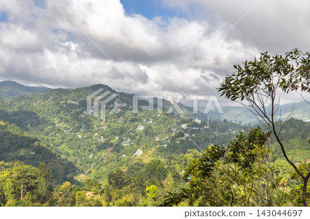 Verdant Mountain Landscape with Scattered Houses Under a Broad, Cloudy Sky on a Bright Day. Mountain landscape near Ella in Sri Lanka. Verdant Mountain Landscape with Scattered Houses Under a Broad, Cloudy Sky on a Bright Day. Mountain landscape near Ella in Sri Lanka. 143044697