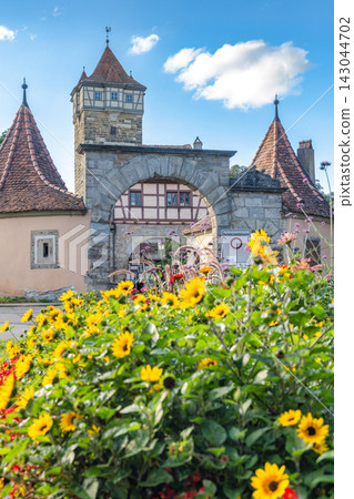 Rothenburg ob der Tauber, medieval old town in region of Bavaria in Germany, Europe. Charming European Architecture and Vibrant Garden Flowers Under Blue Sky on Sunny Day 143044702