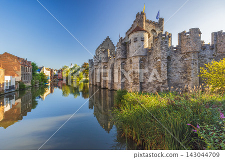 Gravensteen, a medieval castle in the city of Ghent in Belgium, Europe. Historic Stone Castle and Water Reflection in Charming European Canal City under Clear Blue Sky Gravensteen, a medieval castle in the city of Ghent in Belgium, Europe. Historic Stone Castle and Water Reflection in Charming European Canal City under Clear Blue Sky 143044709