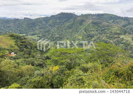 Lush Tropical Hills and Valleys Landscape with Distant Structure Under Cloudy Sky, Abundant Greenery. Mountain landscape near Ella town in Sri Lanka island in Asia. 143044718