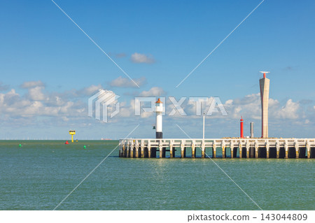 Bright coastal view with historic lighthouse and modern pier structure against a clear sky, guiding ships and defining the horizon. Ostend, a coastal city in Belgium, Europe. 143044809