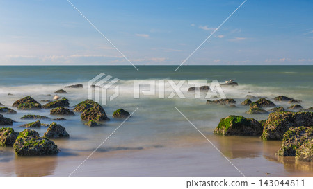 Tranquil Coastal Scene with Moss-Covered Rocks and Serene Sea Water Under a Clear Blue Sky at Sunset or Sunrise Time. Ostend, a coastal city in Belgium, Europe. Tranquil Coastal Scene with Moss-Covered Rocks and Serene Sea Water Under a Clear Blue Sky at Sunset or Sunrise Time. Ostend, a coastal city in Belgium, Europe. 143044811