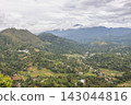 Panoramic view of lush green mountain landscape with distant peaks shrouded in clouds under a dramatic sky. Mountain landscape near Ella town in Sri Lanka island in Asia. 143044816
