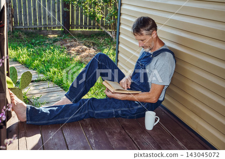 Mature man relaxing on porch while reading book Mature man relaxing on porch while reading book 143045072