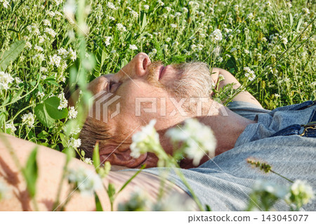 Mature man relaxing in wildflowers, lying on his back and looking at sky 143045077