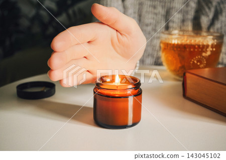 Woman warming her hand over candle with tea and book 143045102