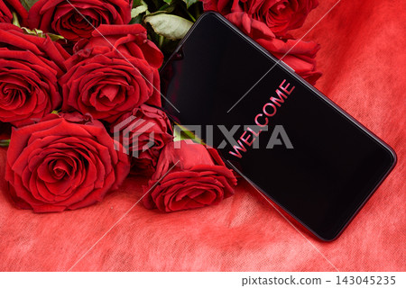 Smartphone with Welcome Text on Screen Lying on Red Roses Bouquet Smartphone with Welcome Text on Screen Lying on Red Roses Bouquet 143045235