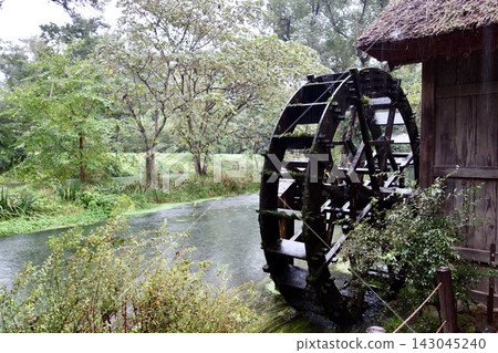 An old-fashioned thatched-roof watermill quietly turning by the water's edge on a rainy day. An old-fashioned thatched-roof watermill quietly turning by the water's edge on a rainy day. 143045240