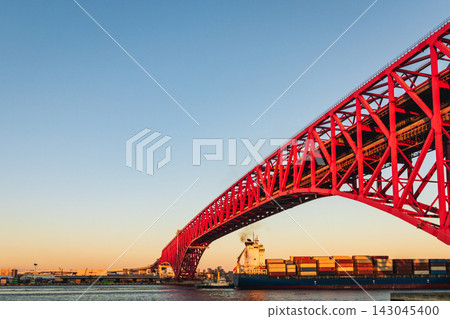 A large bridge glowing red at dusk, and cargo ships carrying goods. A large bridge glowing red at dusk, and cargo ships carrying goods. 143045400