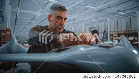 Male Technician Routing Wires Through Fixed Wing UAV Fuselage During Precision Drone Assembly Male Technician Routing Wires Through Fixed Wing UAV Fuselage During Precision Drone Assembly 143046861