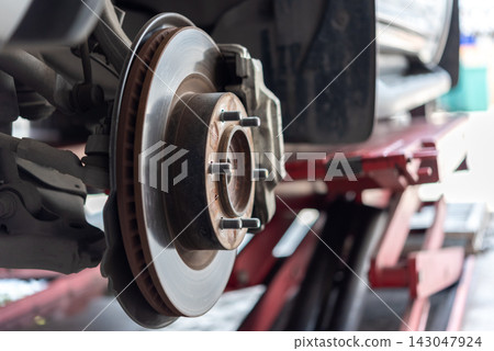 Exposed car disc brake assembly wheel removed showing brake rotor caliper hub suspension components during vehicle maintenance an automotive workshop Exposed car disc brake assembly wheel removed showing brake rotor caliper hub suspension components during vehicle maintenance an automotive workshop 143047924