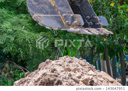 Excavator bucket lifting loose soil rocks at an outdoor worksite surrounded by green vegetation showing earthmoving excavation land development Excavator bucket lifting loose soil rocks at an outdoor worksite surrounded by green vegetation showing earthmoving excavation land development 143047951