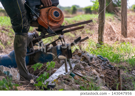 Farm worker handles portable water pump engine beside rural field for irrigation agricultural water management Farm worker handles portable water pump engine beside rural field for irrigation agricultural water management 143047956