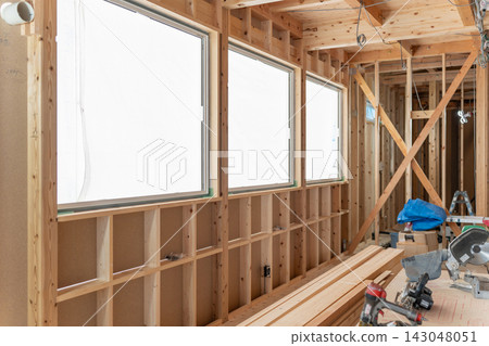 A construction site for a new wooden house. The house is still under construction, with large windows, wall framing, and bracing visible. A construction site for a new wooden house. The house is still under construction, with large windows, wall framing, and bracing visible. 143048051