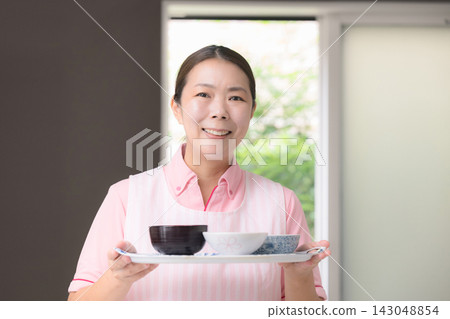 這張圖片描繪了女性工作人員提供餐食,這是家政服務的一部分,包括家庭護理、家庭幫手以及提供日常生活、烹飪和膳食準備方面幫助的人員。 這張圖片描繪了女性工作人員提供餐食,這是家政服務的一部分,包括家庭護理、家庭幫手以及提供日常生活、烹飪和膳食準備方面幫助的人員。 143048854