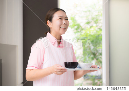 這張圖片描繪了女性工作人員提供餐食,這是家政服務的一部分,包括家庭護理、家庭幫手以及提供日常生活、烹飪和膳食準備方面幫助的人員。 這張圖片描繪了女性工作人員提供餐食,這是家政服務的一部分,包括家庭護理、家庭幫手以及提供日常生活、烹飪和膳食準備方面幫助的人員。 143048855