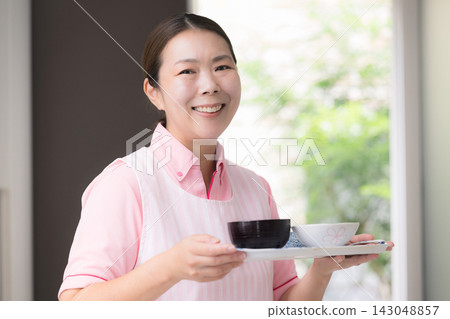 這張圖片描繪了女性工作人員提供餐食,這是家政服務的一部分,包括家庭護理、家庭幫手以及提供日常生活、烹飪和膳食準備方面幫助的人員。 這張圖片描繪了女性工作人員提供餐食,這是家政服務的一部分,包括家庭護理、家庭幫手以及提供日常生活、烹飪和膳食準備方面幫助的人員。 143048857