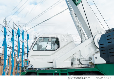 A crane working at a wooden house construction site. A crane operator supporting the roof framing. A crane working at a wooden house construction site. A crane operator supporting the roof framing. 143048872