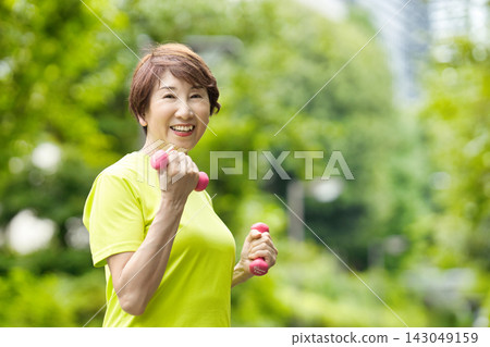 一位微笑的老婦人手持粉紅色啞鈴。 一位微笑的老婦人手持粉紅色啞鈴。 143049159