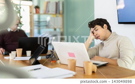 Wearied senior man and guy colleagues are dozing near workplace in office Wearied senior man and guy colleagues are dozing near workplace in office 143049898