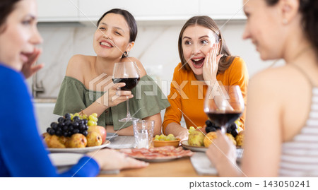 Four women are sitting at table, enjoying food and wine, chatting, talking, laughing. Four women are sitting at table, enjoying food and wine, chatting, talking, laughing. 143050241