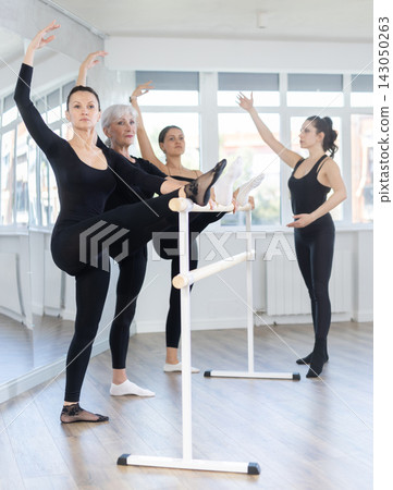 Female ballet teacher showing moves in front of group of different aged dancers in dancing studio. Ballet pose grand batman Female ballet teacher showing moves in front of group of different aged dancers in dancing studio. Ballet pose grand batman 143050263